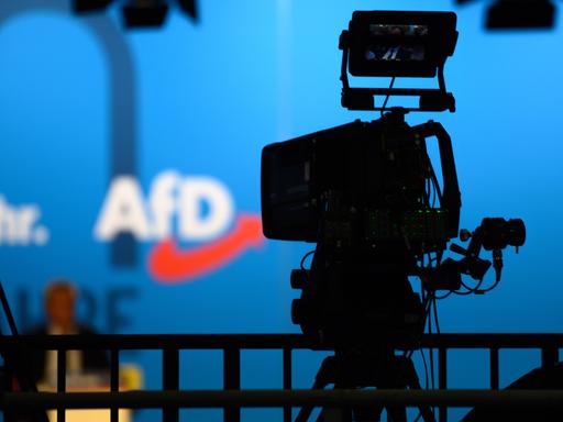 Eine Fernsehkamera steht auf der AfD-Europawahlversammlung auf einem Podium. Im Hintergrund sieht man das Logo der Partei.