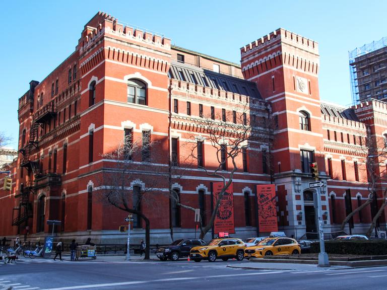 Das wie eine Ritterburg mit Türmen gestaltete Park Avenue Armory Center, davor stehen Autos an einer Kreuzung.