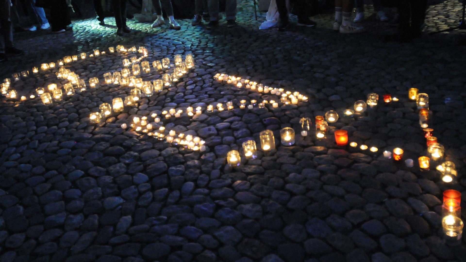 Windlichter mit brennenden Kerzen auf einem Platz formen das Wort "Gaza".