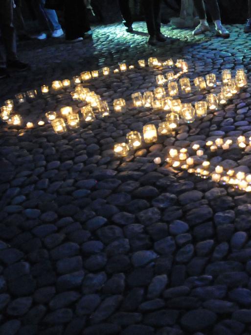 Windlichter mit brennenden Kerzen auf einem Platz formen das Wort "Gaza".