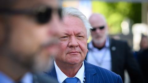 Der grauhaarige Papperger vor anderen Personen im Freien. Im Vordergrund unscharf ein Kopf mit Brille.
