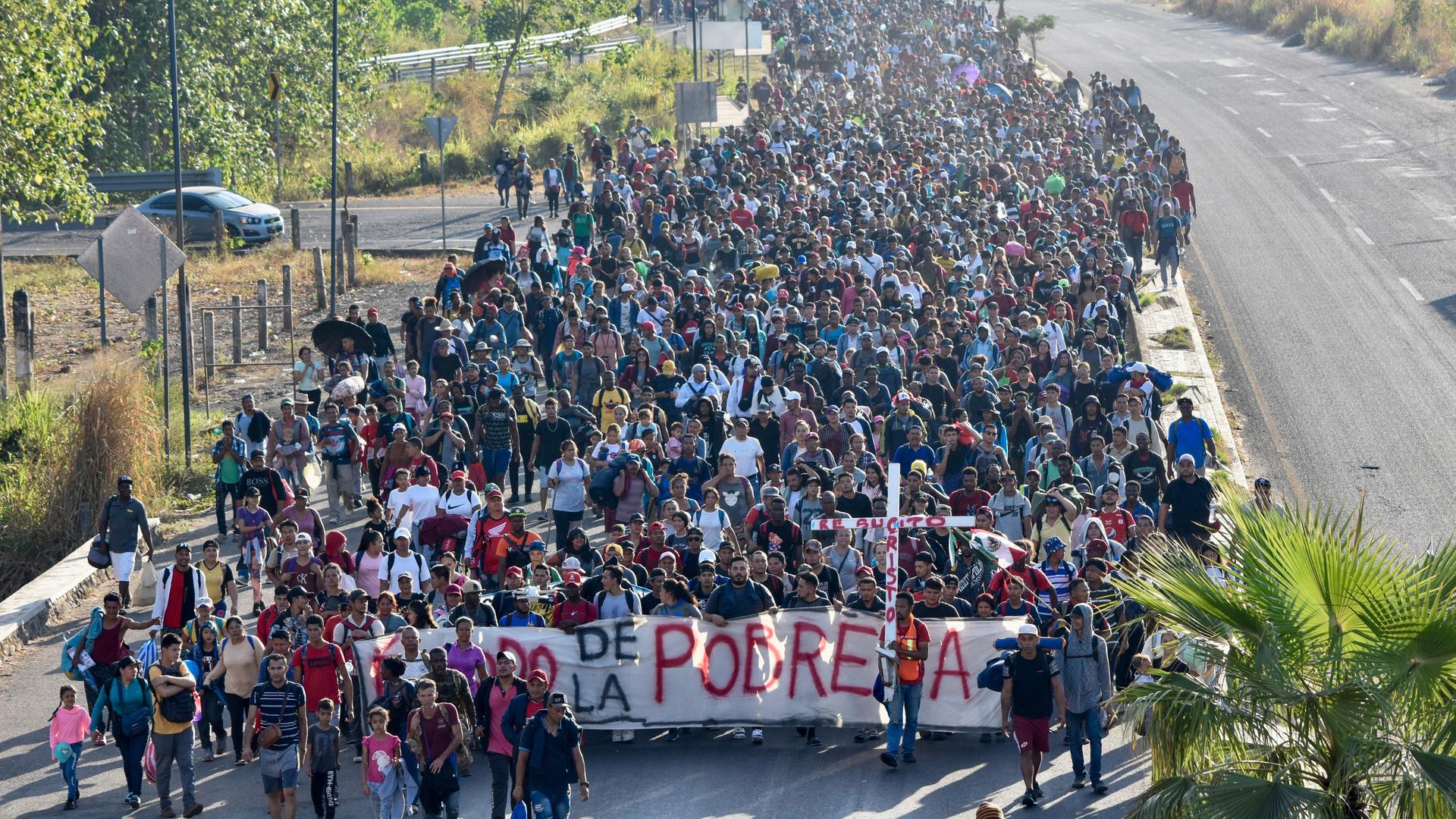 Tausende Migranten laufen auf einer breiten Straße.