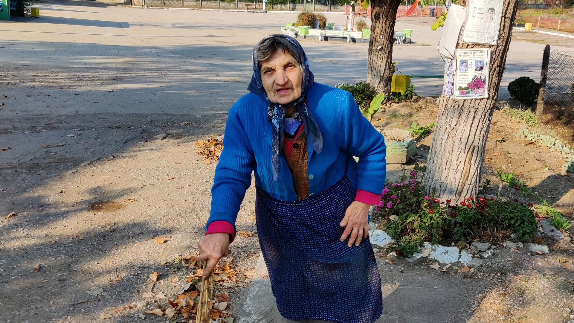 Eine alte Frau mit einem Besen auf einer Strasse.