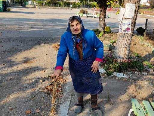 Eine alte Frau mit einem Besen auf einer Strasse.