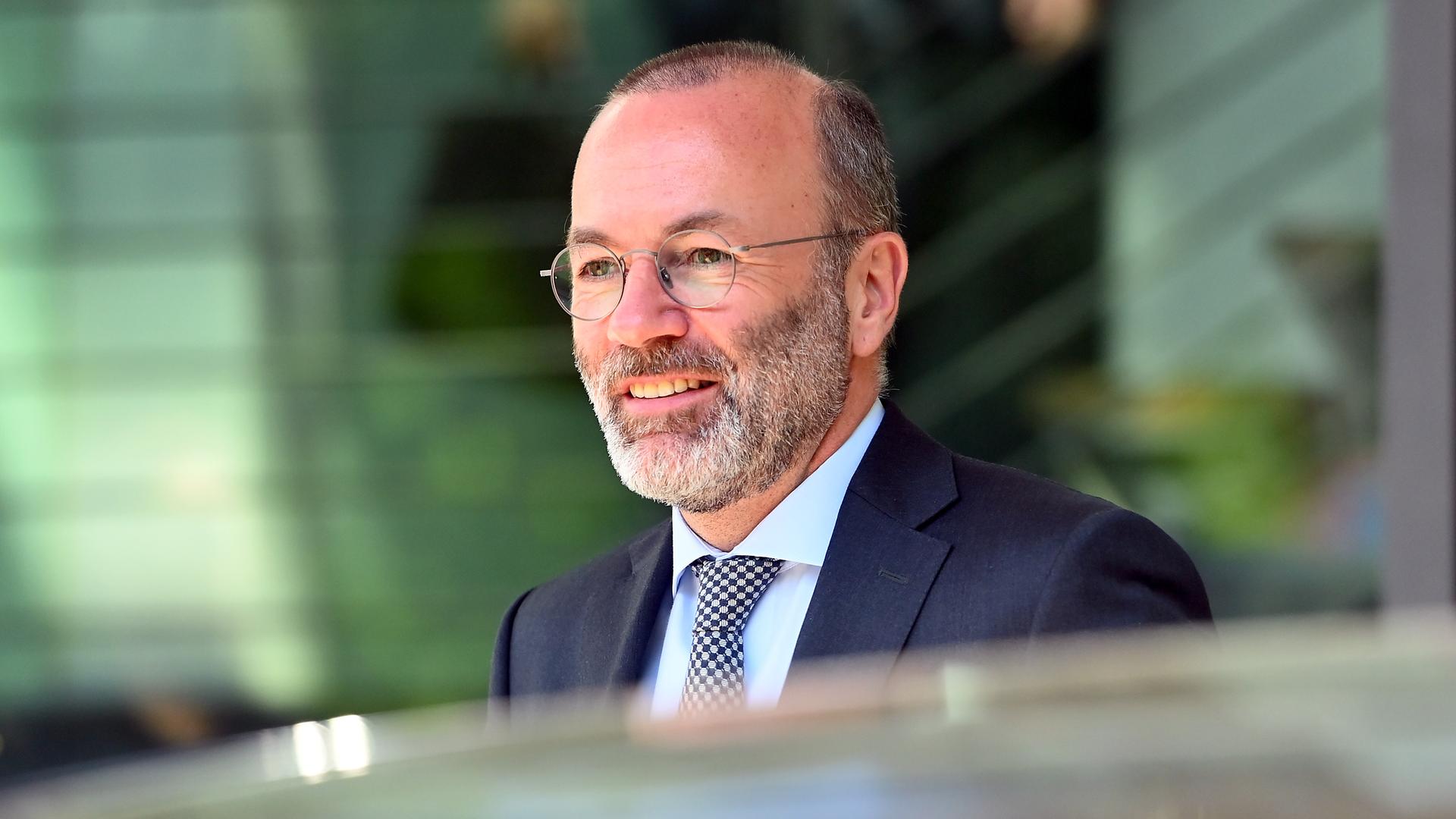 Manfred Weber läuft lächelnd an den Fotografen vorbei. Er trägt Brille und eine dunkle Anzugjacke. 