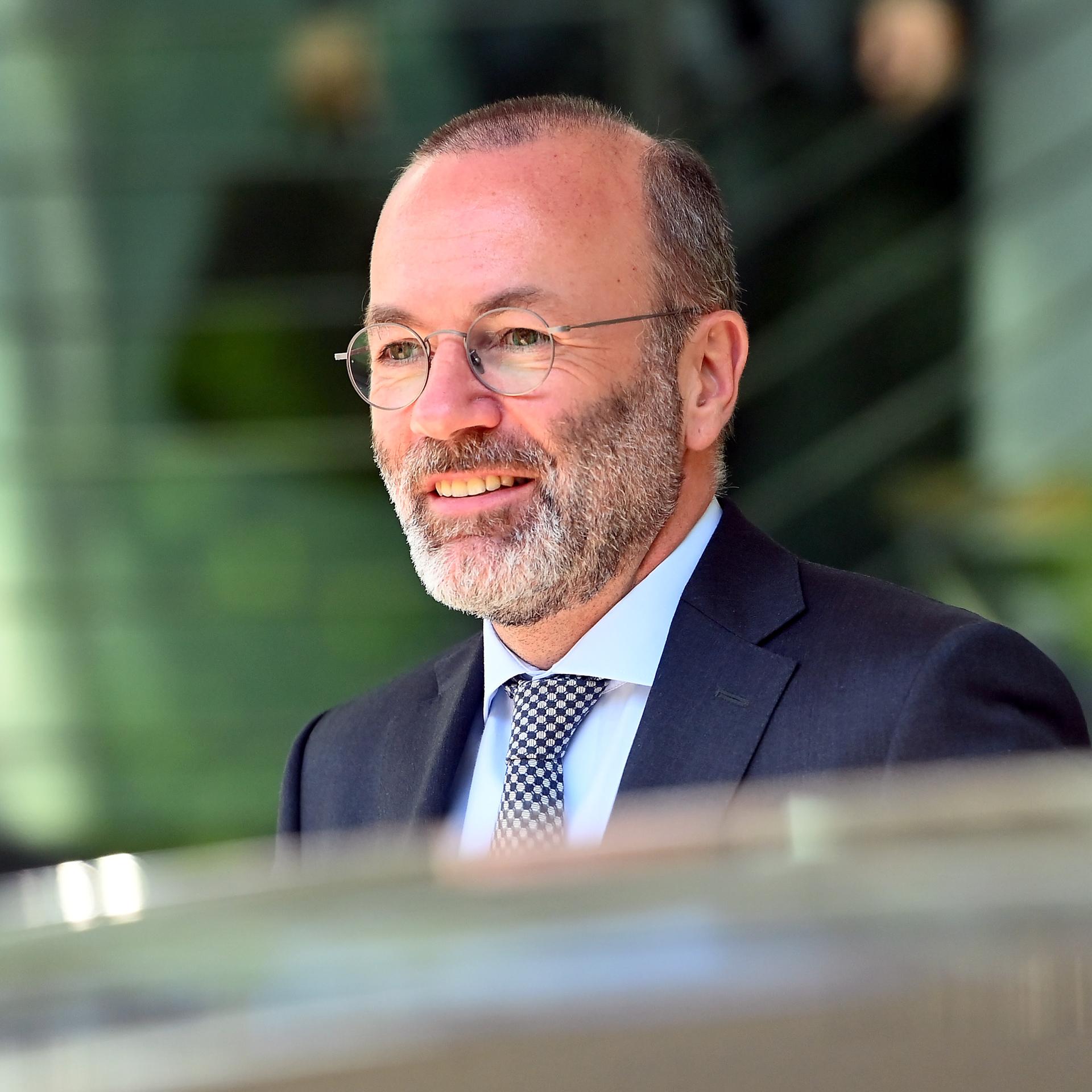 Manfred Weber läuft lächelnd an den Fotografen vorbei. Er trägt Brille und eine dunkle Anzugjacke. 
