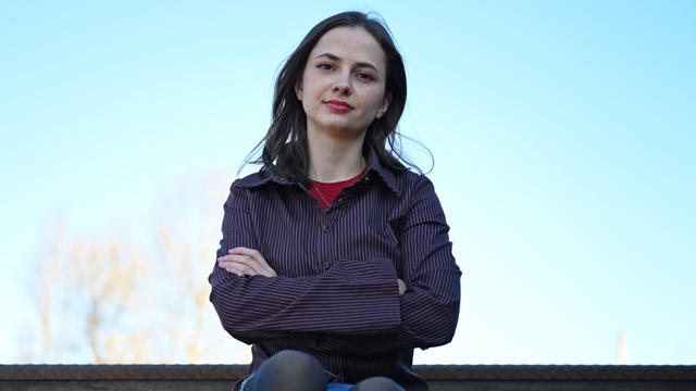 Theresia Crone sitzt im Park am Gleisdreieck in Berlin. Vor blauem Himmel im Hintergrund hält sie die Arme verschränkt und blickt direkt in die Kamera.