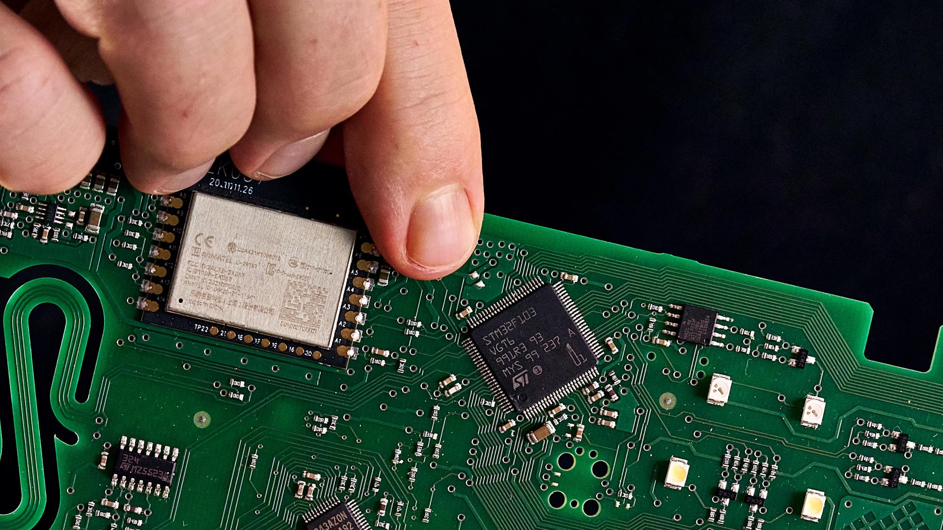 Person hält eine Leiterplatine mit elektronischen Chips in der Hand.  Person hält eine Leiterplatine mit elektronischen Chips in der Hand.
