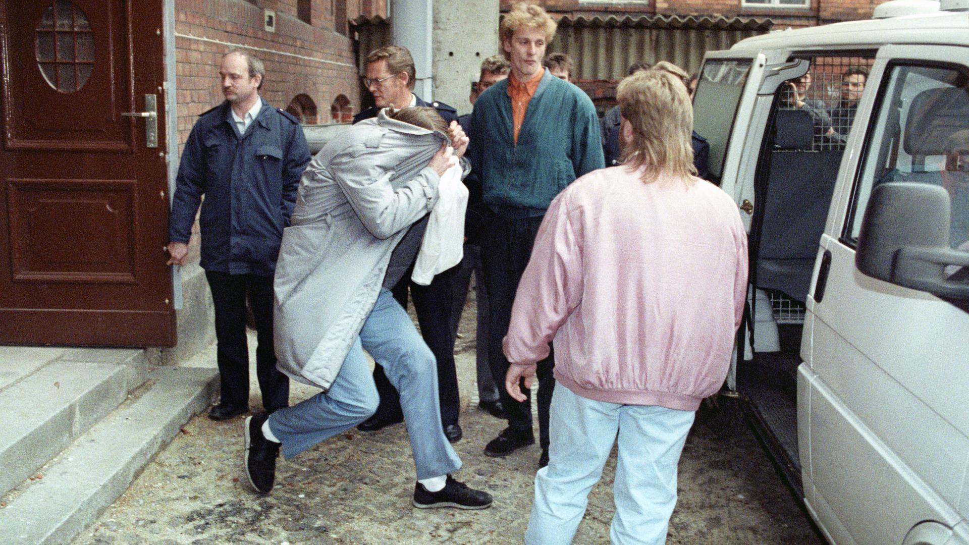 Wolfgang Schmidt zieht am 30. November 1992 beim Verlassen des Gerichtssaals den Mantel über den Kopf. Weitere Personen sichern den Einstieg ins Auto ab.