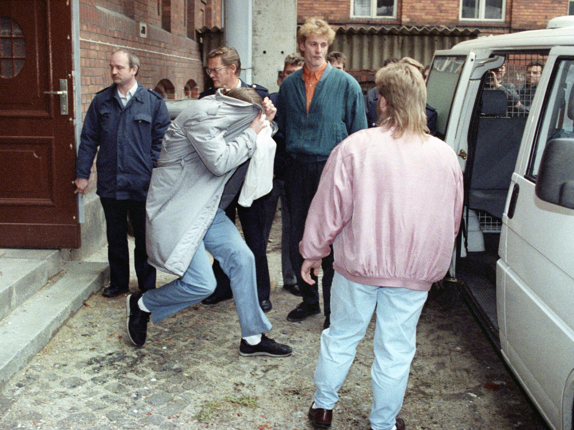 Eine historische Aufnahme vom 30. November 1992 zeigt den Mörder Wolgang Schmidt beim Verlassen des Gerichtsgebäudes. Sein Gesicht ist von einem Mantel verdeckt. Weitere Personen sichern den Einstieg in ein Auto ab.