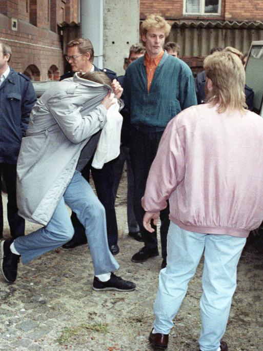 Wolfgang Schmidt zieht am 30. November 1992 beim Verlassen des Gerichtssaals den Mantel über den Kopf. Weitere Personen sichern den Einstieg ins Auto ab.