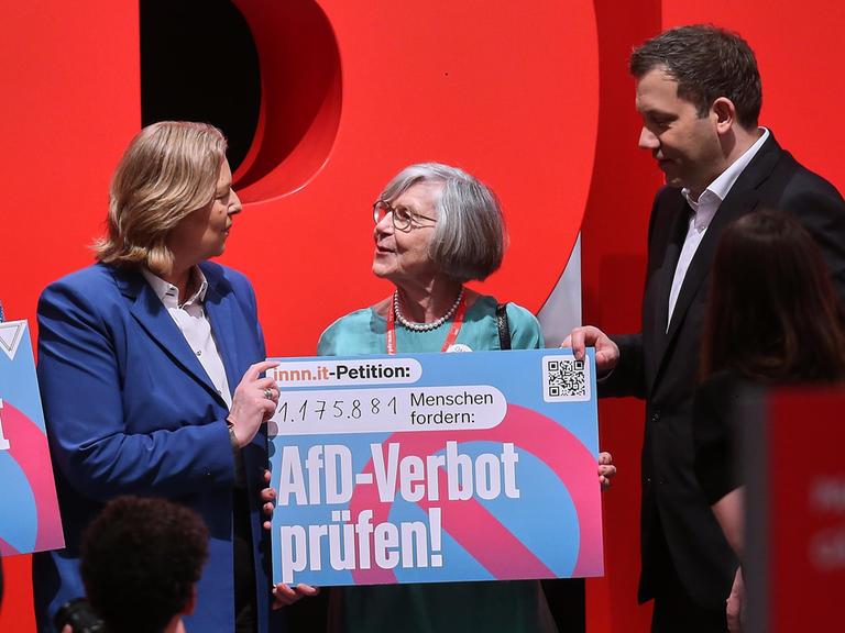 42. SPD-Bundesparteitag: Bundesarbeitsministerin Bärbel Bas und Bundesfinanzminister Lars Klingbeil (SPD) heben mit Betina Kern von 'Omas gegen Rechts' ein Schild zur Prüfung eines AfD-Verbots hoch, auf dem steht: "AfD-Verbot prüfen!"