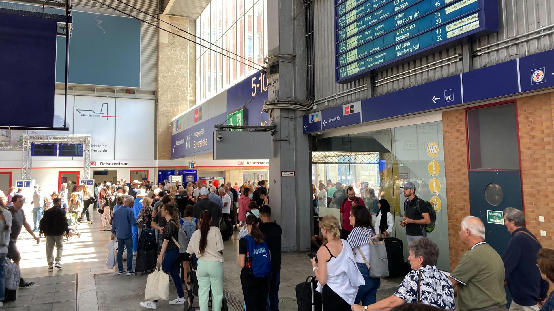 Menschen stehen mit Reisegepäck in einem Bahnhof in der Schlange.