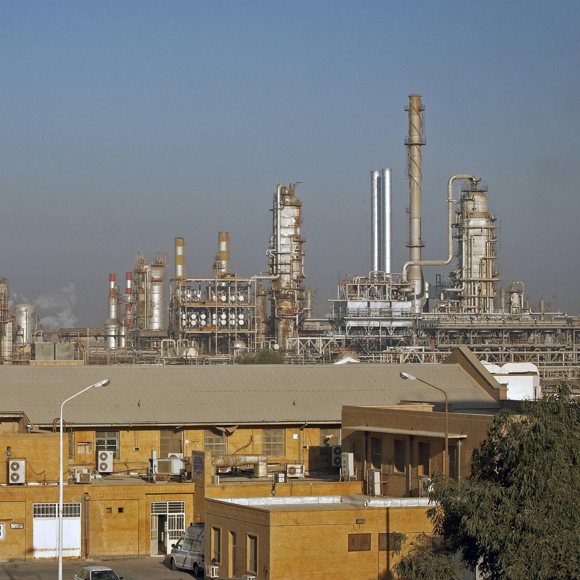 Zu sehen ist eine große Raffinerie mit vielen Türmen und Leitungen. Im Vordergrund ist ein großes Steingebäude. 
