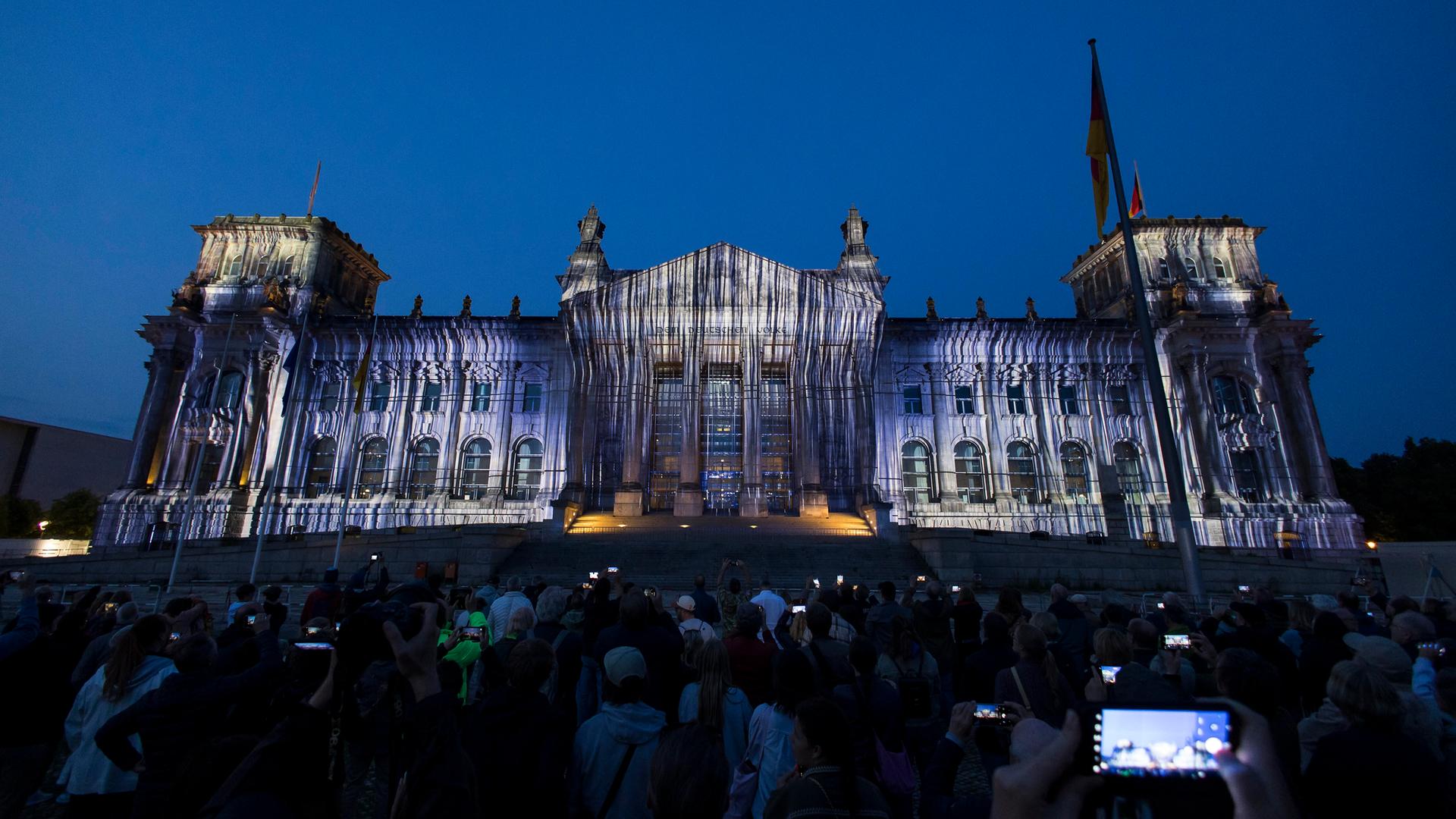 Schaulustige betrachten die abendliche Fassade des Reichstags-Gebäudes in Berlin, auf die Stoff-Bahnen projiziert werden Schaulustige betrachten die abendliche Fassade des Reichstags-Gebäudes in Berlin, auf die Stoff-Bahnen projiziert werden