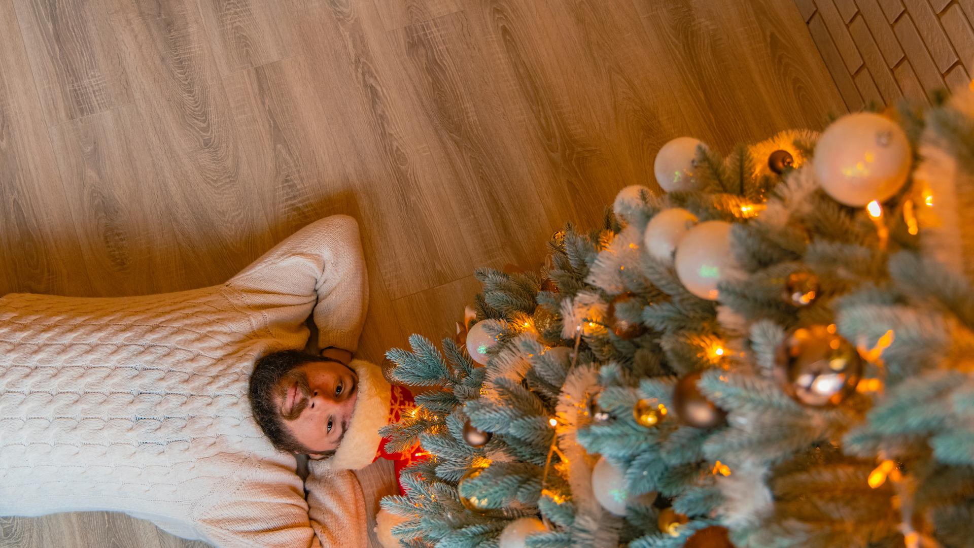 Ein Mann liegt allein neben einem Weihnachtsbaum.