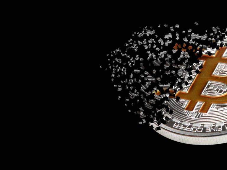 Ein physischer Bitcoin, der zerfällt vor schwarzem Hintergrund.