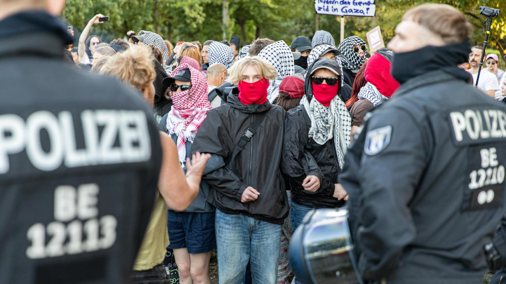 Demonstranten, teils verhüllt mit palästinensischen Keffiyeh, stehen Polizisten in Einsatzmontur gegenüber