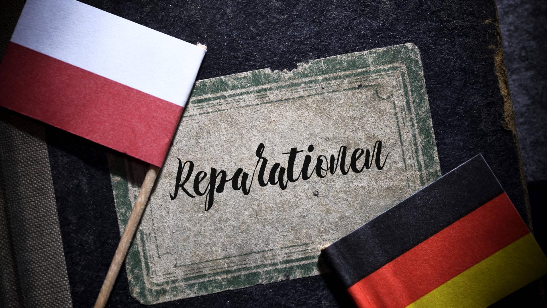 Fahnen von Deutschland und Polen liegen auf einem Buch mit der Aufschrift "Reparationen". (Symbolbild)