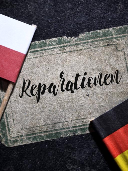 Fahnen von Deutschland und Polen liegen auf einem Buch mit der Aufschrift "Reparationen". (Symbolbild)
