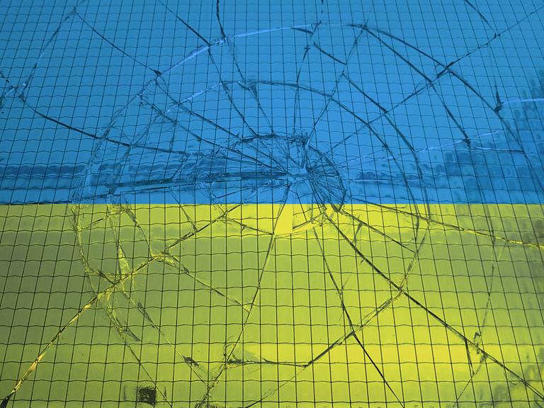 Eine ukrainische Flagge hinter einer zerbrochenen Glasscheibe