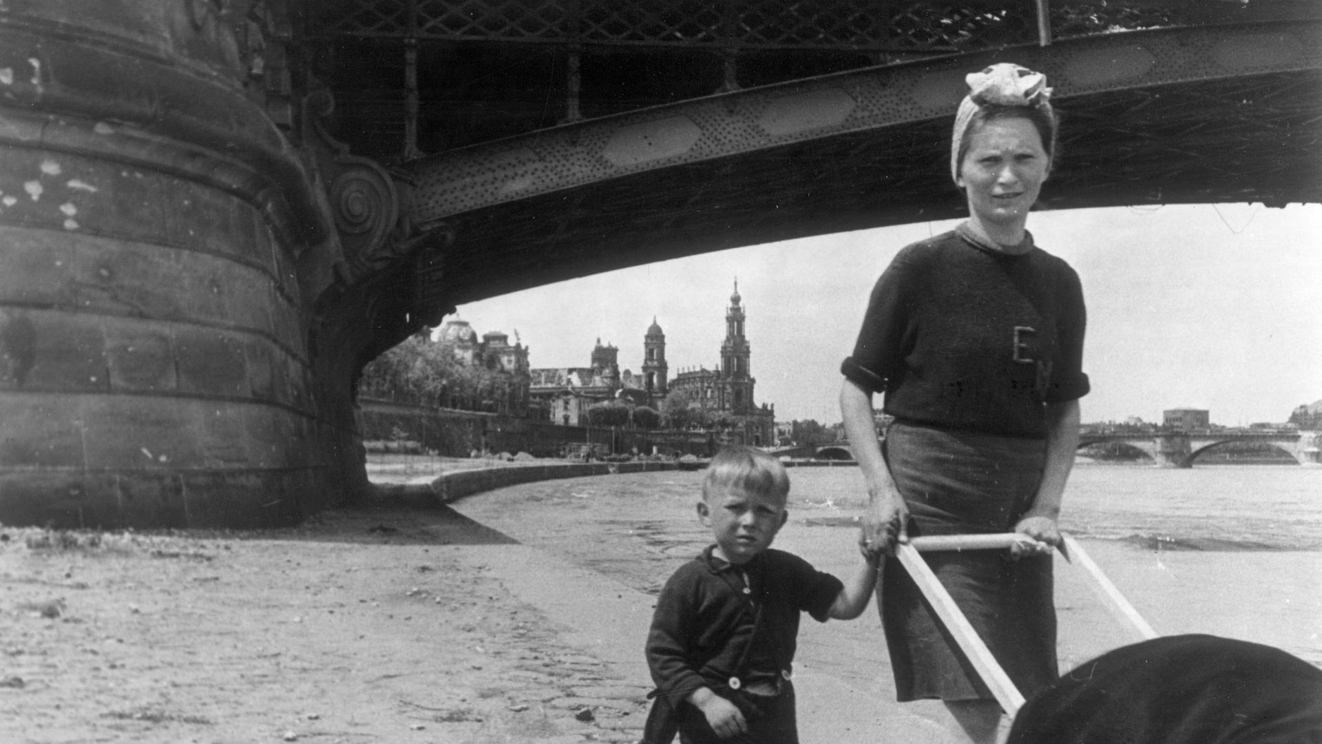 Eine junge Frau hat einen Knaben an der Hand und schiebt einen Kinderwagen an der Elbe in Dresden im Mai 1945.