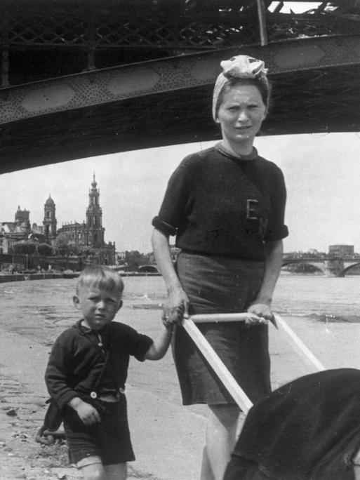 Eine junge Frau hat einen Knaben an der Hand und schiebt einen Kinderwagen an der Elbe in Dresden im Mai 1945.