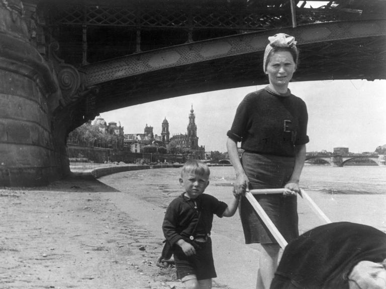 Eine junge Frau hat einen Knaben an der Hand und schiebt einen Kinderwagen an der Elbe in Dresden im Mai 1945.