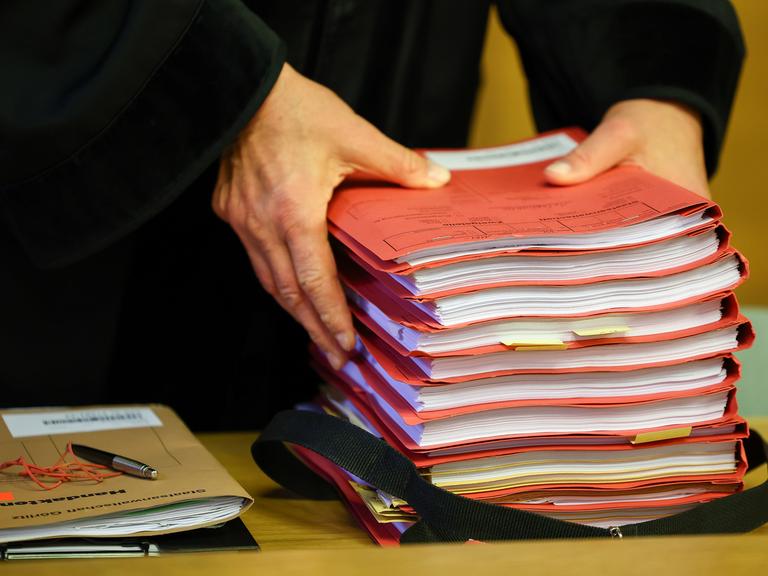 Ein Staatsanwalt legt vor Prozessbeginn einen Stapel Akten auf seinen Tisch.