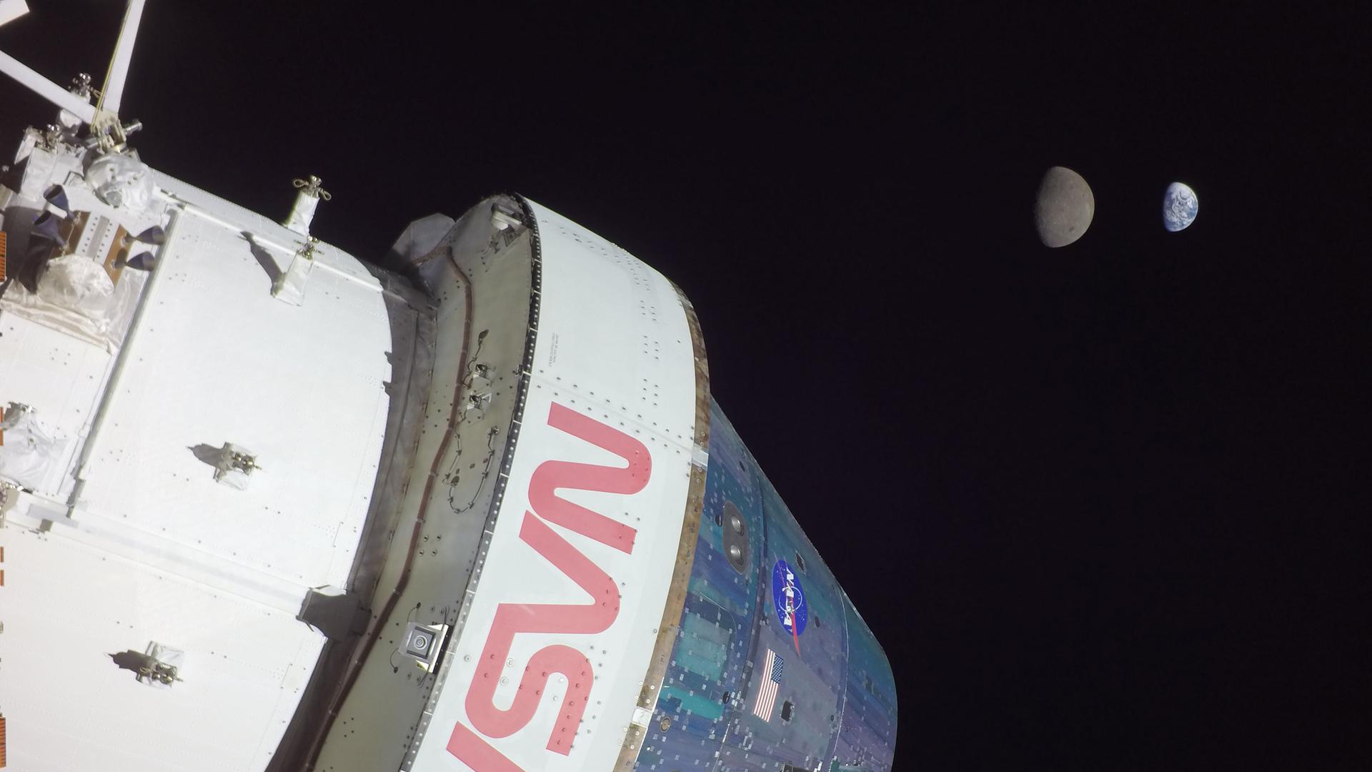 "Artemis"-Mission: Eine Raumkapsel mit NASA-Aufschrift fliegt durchs Weltall. Im Hintergrund sind der Mond und die Erde zu sehen.