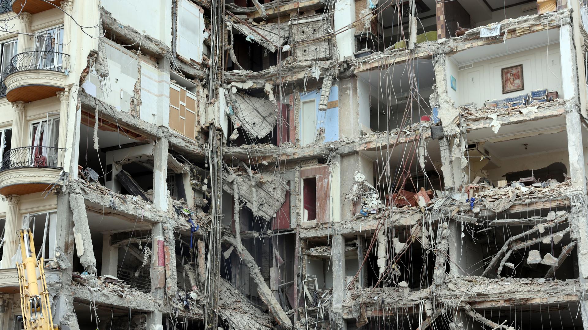 Bei einem mehrstöckigen Haus ist die vordere Wand weggesprengt. Der Blick in verschiedene Etagen ist frei. Im Vordergrund liegt Schutt.