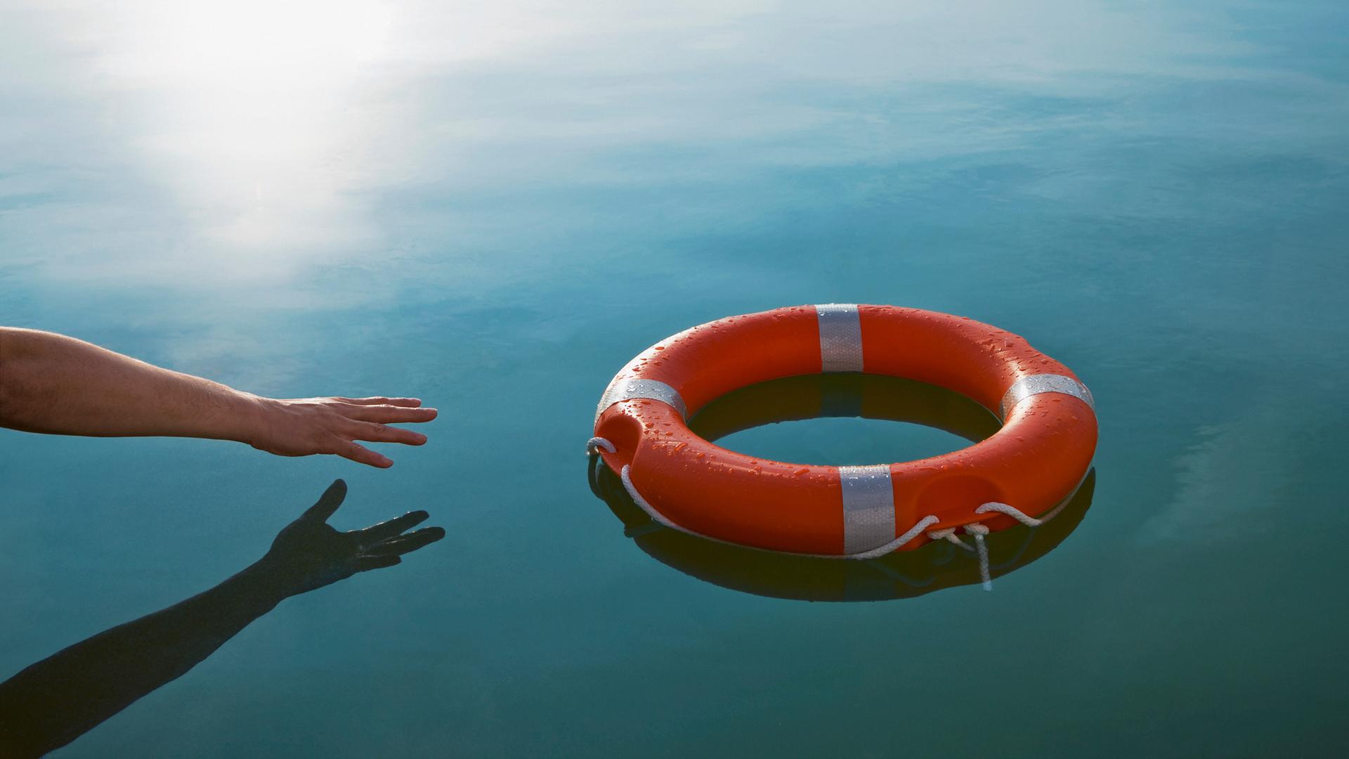 Symbolbild: Eine Hand streckt sich nach einem Rettungsring im Wasser.