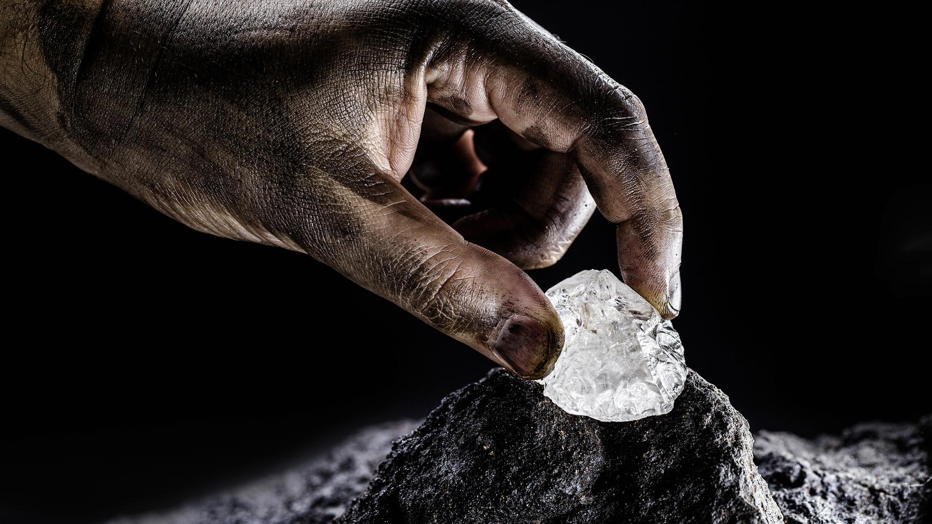 Eine Hand greift einen weiss schimmernden Stein, einen Petalit. Petalit ist ein selten vorkommendes Mineral– eine wichtige Lithiumquelle.