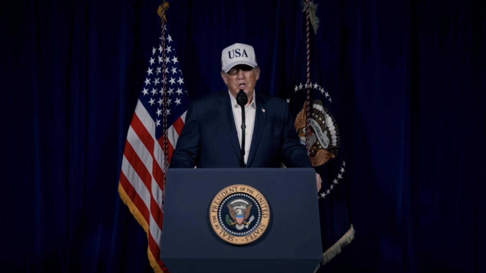 US-Präsident Trump steht an einem Rednerpult. Er trägt eine Kappe mit der Aufschrift USA. US-Präsident Trump steht an einem Rednerpult. Er trägt eine Kappe mit der Aufschrift USA.