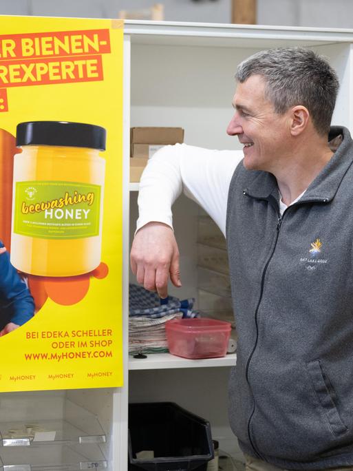 Der Imker Rico Heinzig steht neben einem Plakat mit dem Foto des Moderators Jan Böhmermann. Darauf steht: "Führender Bienen- und Käferexperte empfiehlt." Daneben ist ein Glas Honig mit der Aufschrift "beewashing Honey" zu sehen.