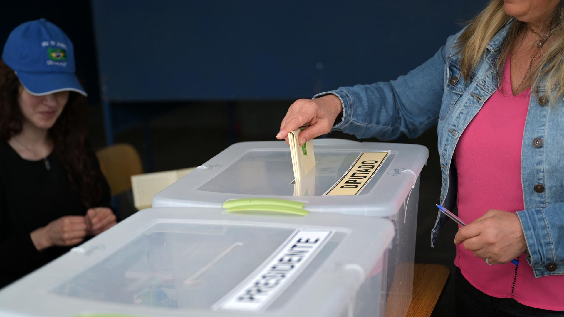 Eine Frau steckt in einem Wahllokal ihren Stimmzettel in eine Box. Man sieht ihren Kopf nicht. Eine Frau steckt in einem Wahllokal ihren Stimmzettel in eine Box. Man sieht ihren Kopf nicht.