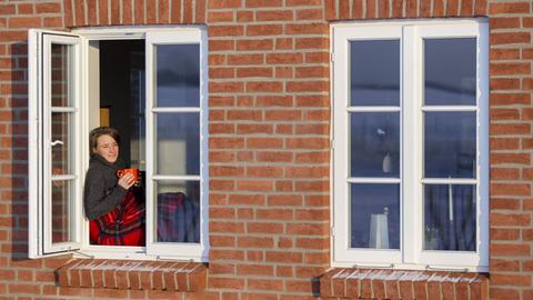 Gemütliches Barnstedt: Junge Frau sitzt auf einem Fensterbrett mit Wolldecke und Kaffeetasse in der Hand