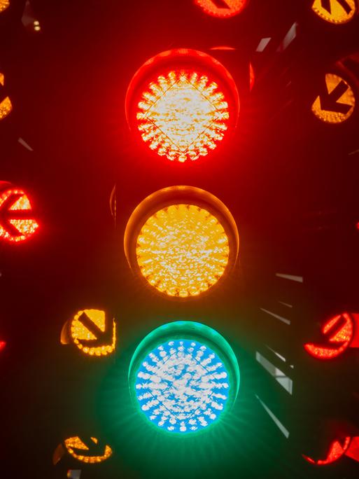 Eine Langzeitbelichtung einer Ampel bei Nacht, die in allen Phasen  Rot, Gelb und Grün leuchtet.