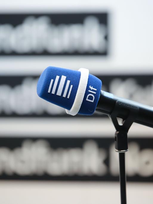 Mikrofon mit Deutschlandfunk-Windschutz vor einer Wand mit den Logos der Sender Deutschlandfunk, Deutschlandfunk Kultur und Deutschlandfunk Nova