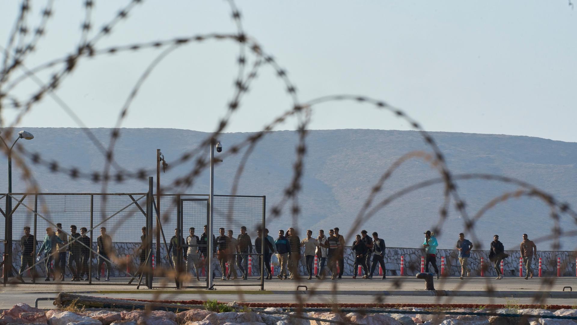 Blick durch einen Stacheldrahtzaun auf eine Gruppe Geflüchtete bei ihrer Ankunft in Griechenland Blick durch einen Stacheldrahtzaun auf eine Gruppe Geflüchtete bei ihrer Ankunft in Griechenland