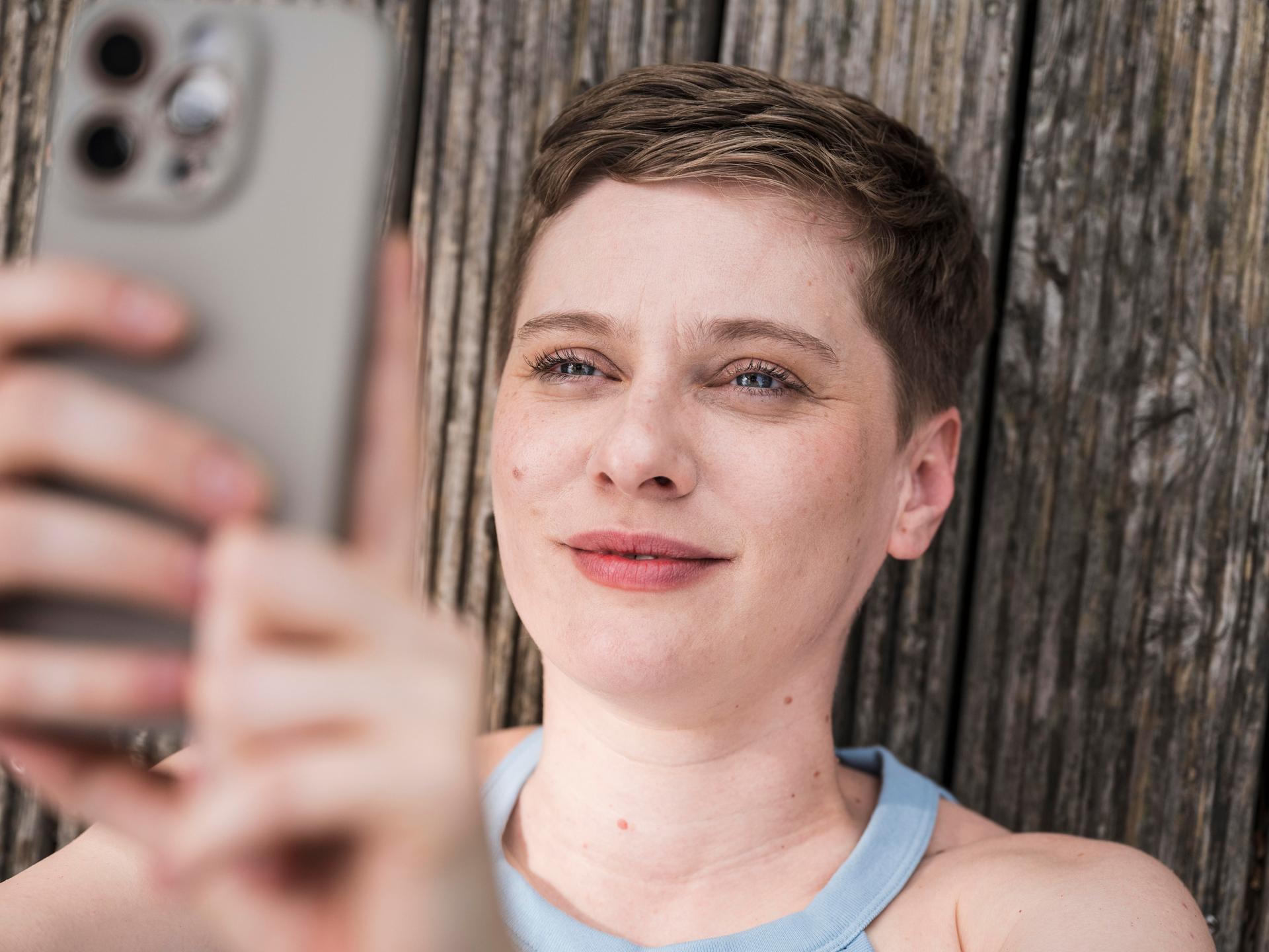 Eine junge Frau blickt lächelnd in ihr Smartphone.