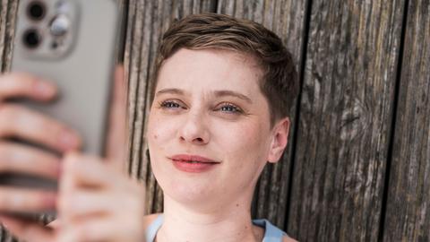 Eine junge Frau blickt lächelnd in ihr Smartphone. Eine junge Frau blickt lächelnd in ihr Smartphone.