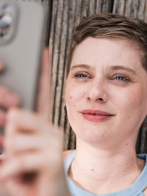 Eine junge Frau blickt lächelnd in ihr Smartphone. Eine junge Frau blickt lächelnd in ihr Smartphone.