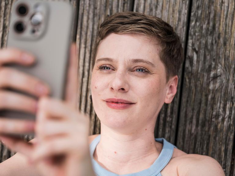 Eine junge Frau blickt lächelnd in ihr Smartphone. Eine junge Frau blickt lächelnd in ihr Smartphone.