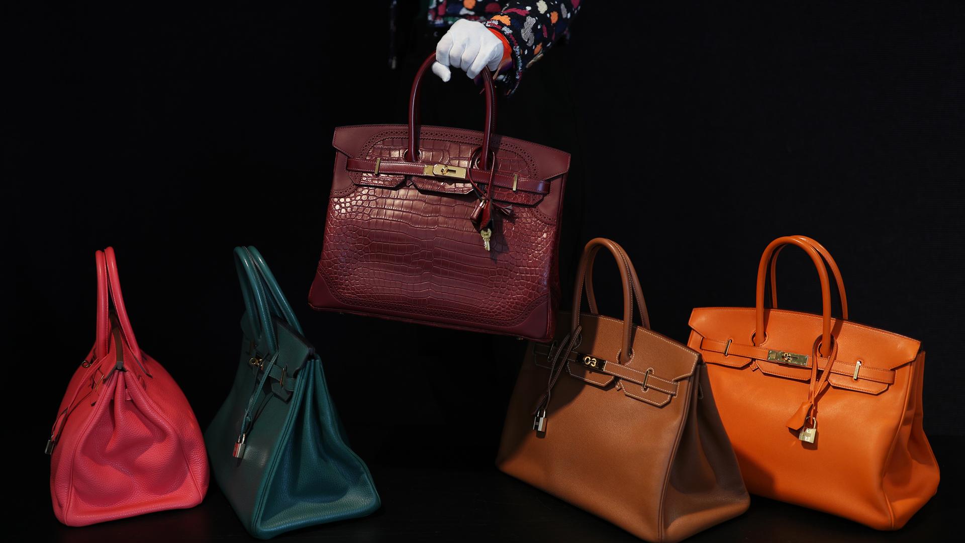 Auf einem schwarzen Hintergrund werden fünf Birkin Bags in verschiedenen Farben und Materialien präsentiert.