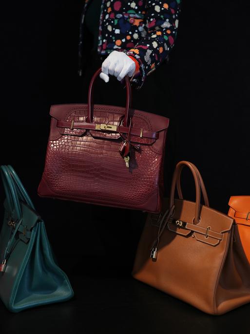 Auf einem schwarzen Hintergrund werden fünf Birkin Bags in verschiedenen Farben und Materialien präsentiert.