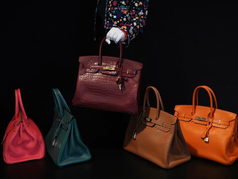 Auf einem schwarzen Hintergrund werden fünf Birkin Bags in verschiedenen Farben und Materialien präsentiert.