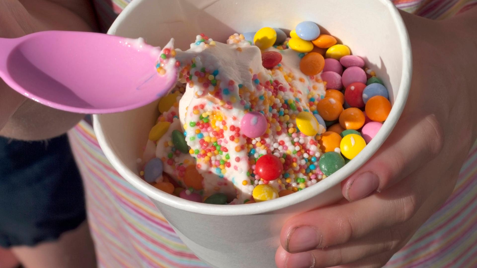 Ein bunter Eisbecher mit Smarties in Kinderhand.