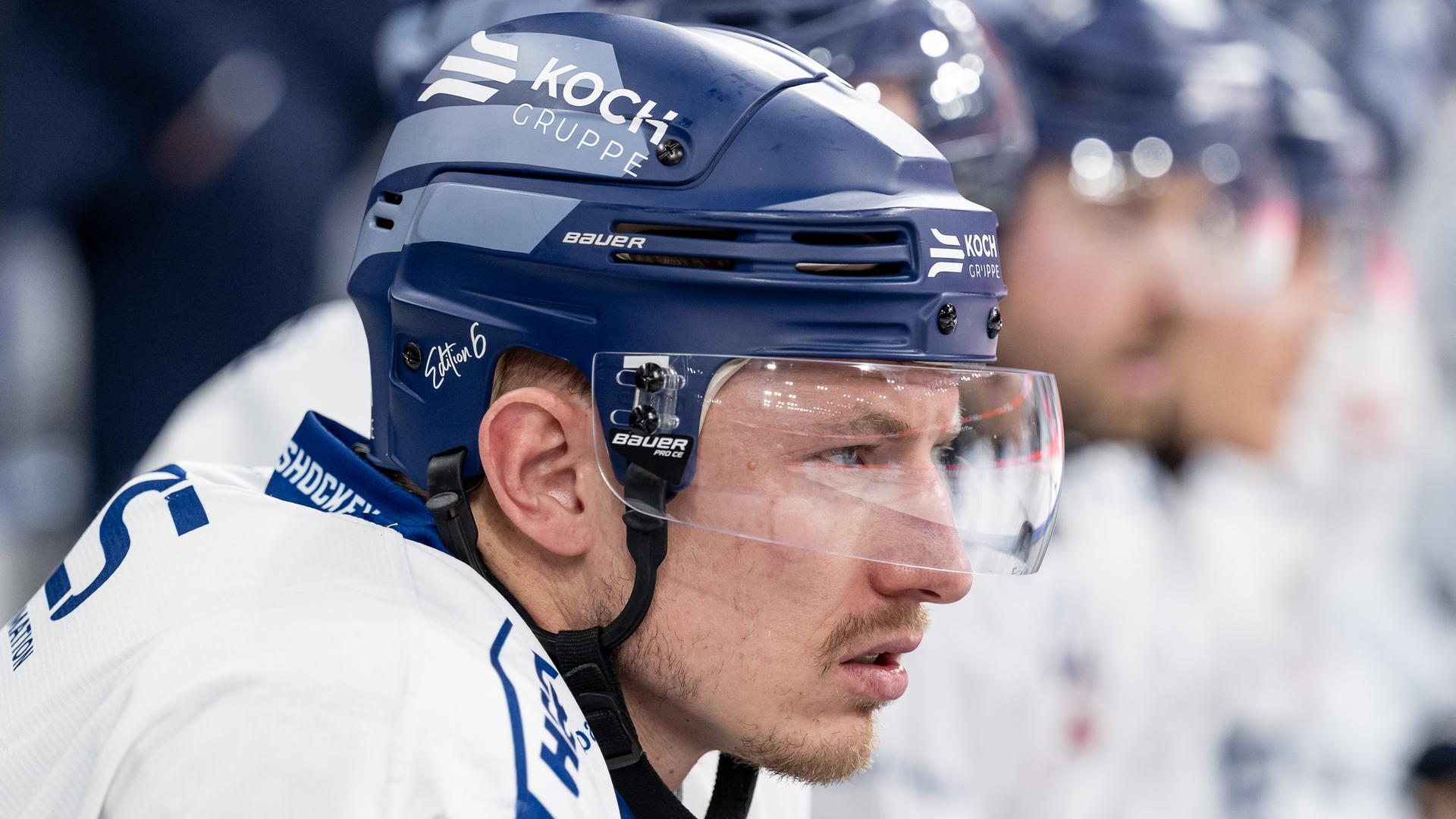 Eishockeyspieler Marcel Brand im Profil. Er hat einen blauen Helm mit Augenschutz auf und trägt ein weiß-blaues Trikot.