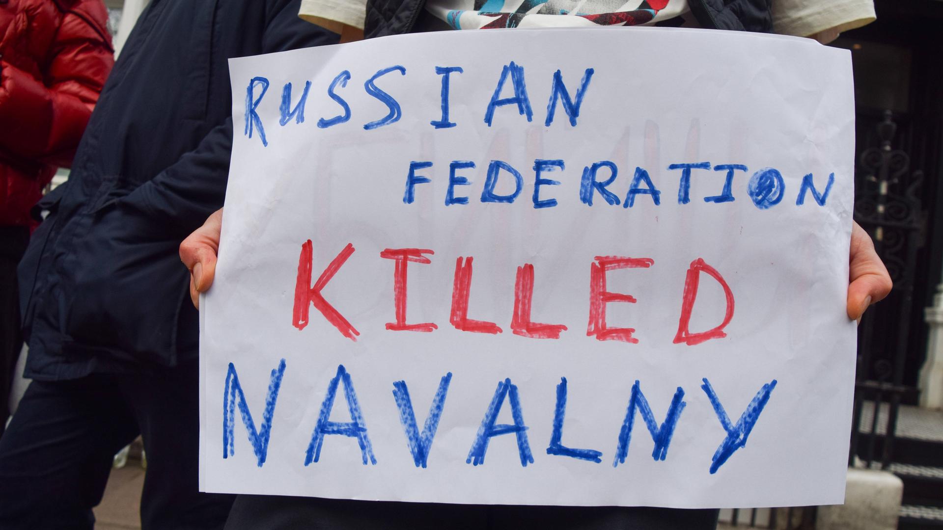 Vor der russischen Botschaft in London haben kurz nach der Meldung über Nawalnys Tod Menschen protestiert. Einer hält ein Schild mit der Aufschrift: "Russian Federation killed Nawalny".